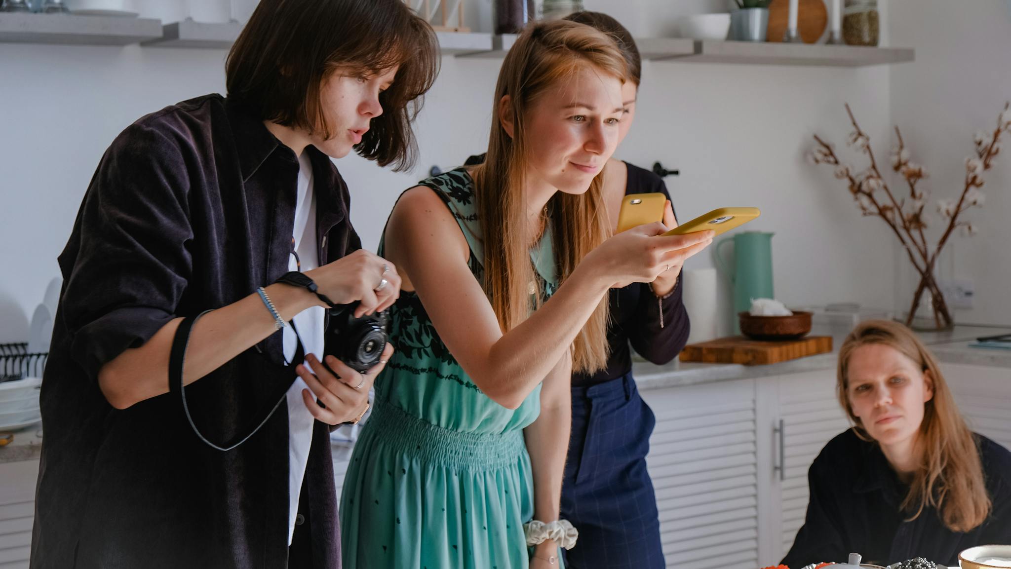 Three women engaged in a creative photography session inside a modern kitchen.